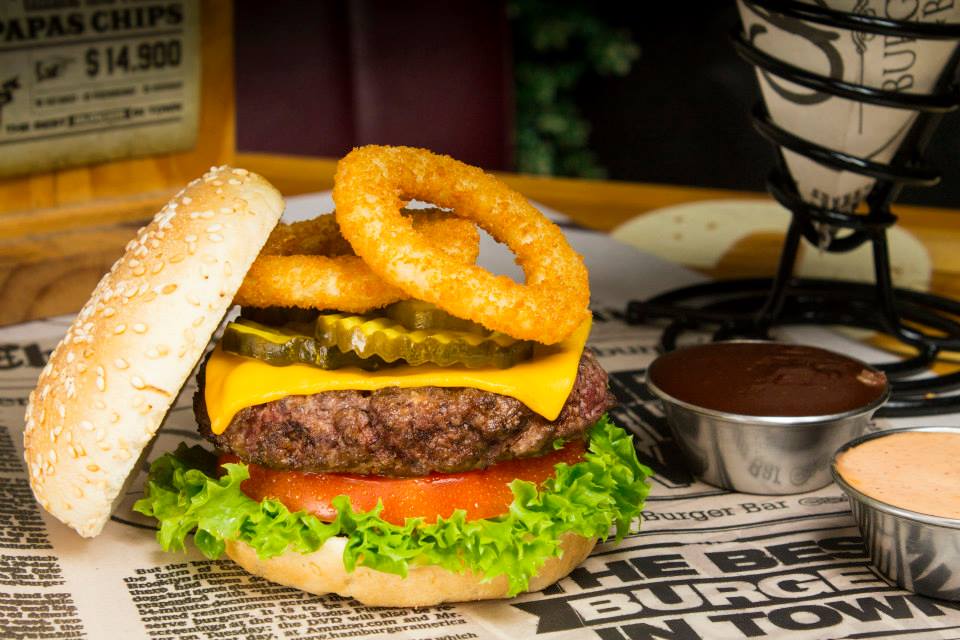 A hamburger with onion rings and pickles on top of it.